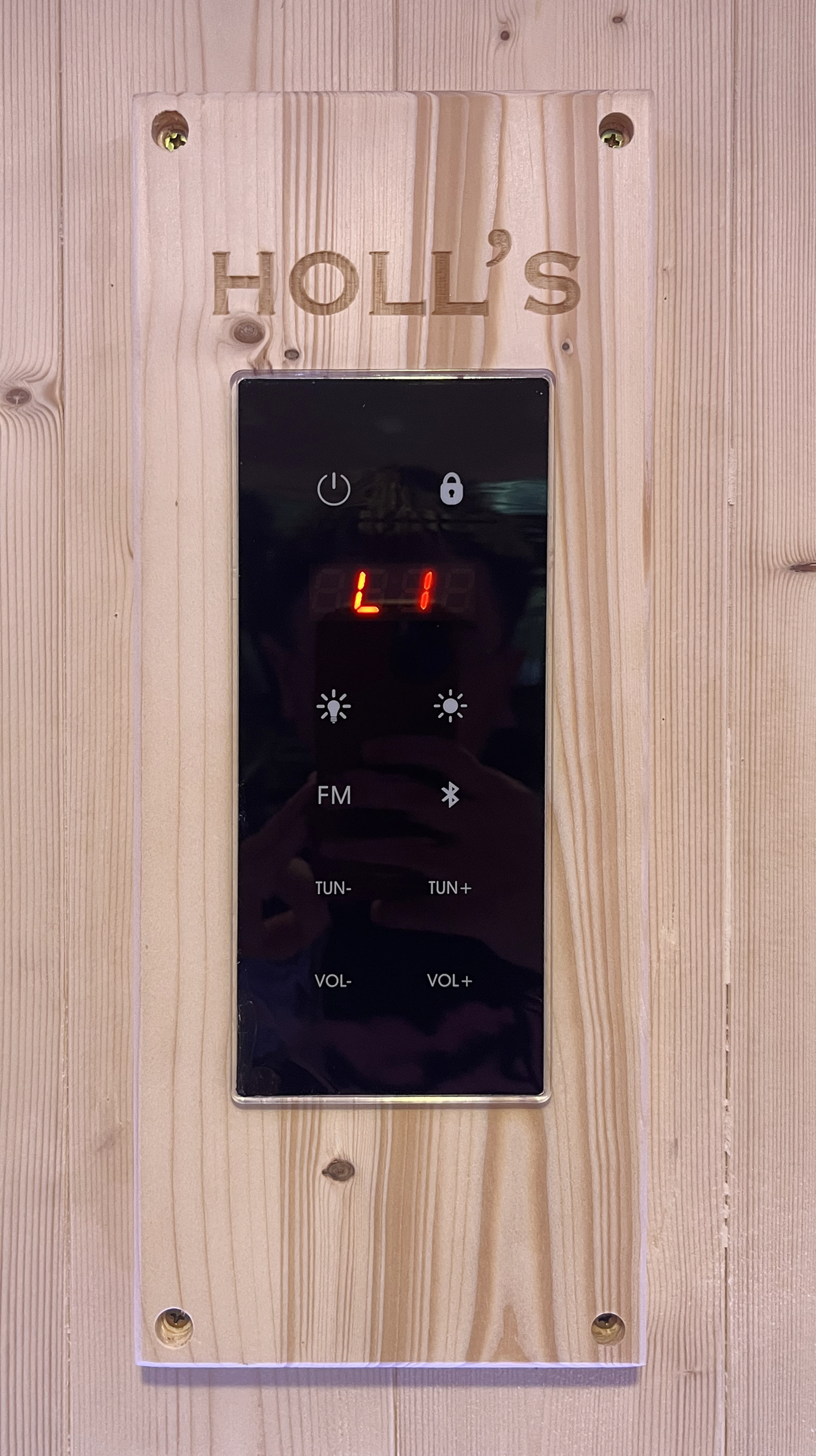Panneau de commande noir brillant pour sauna, monté sur une surface en bois.